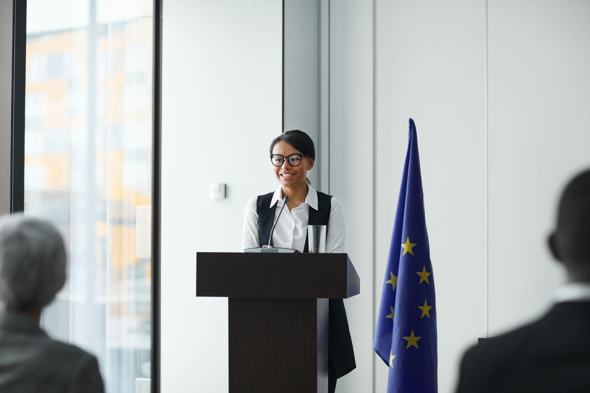 A woman giving a speech at a podium in a conference setting.